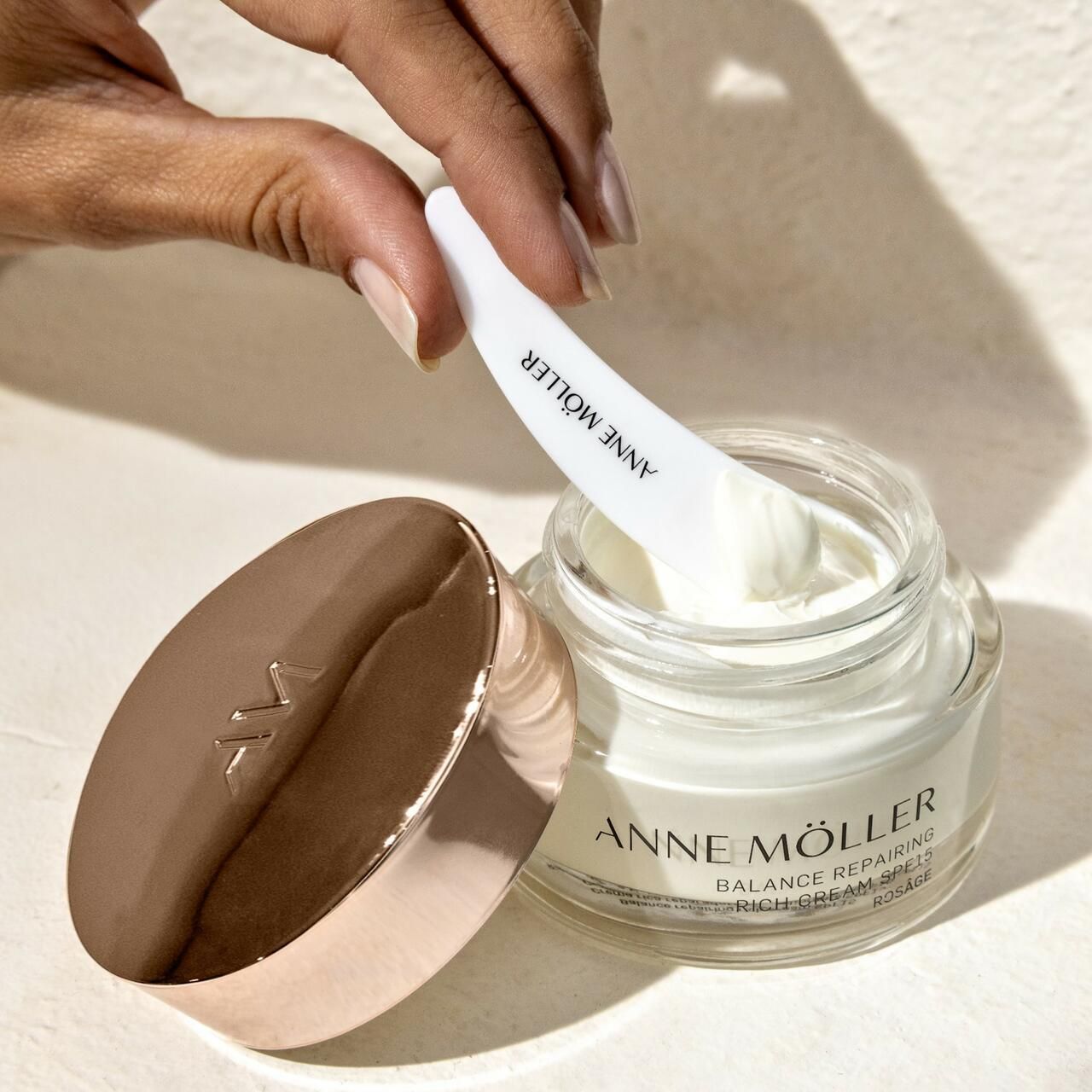 Vasetto di crema con spatola. Scritta: ANNE MÖLLER, Balance Repairing Rich Cream SPF15, Rosâge. Spatola in mano.