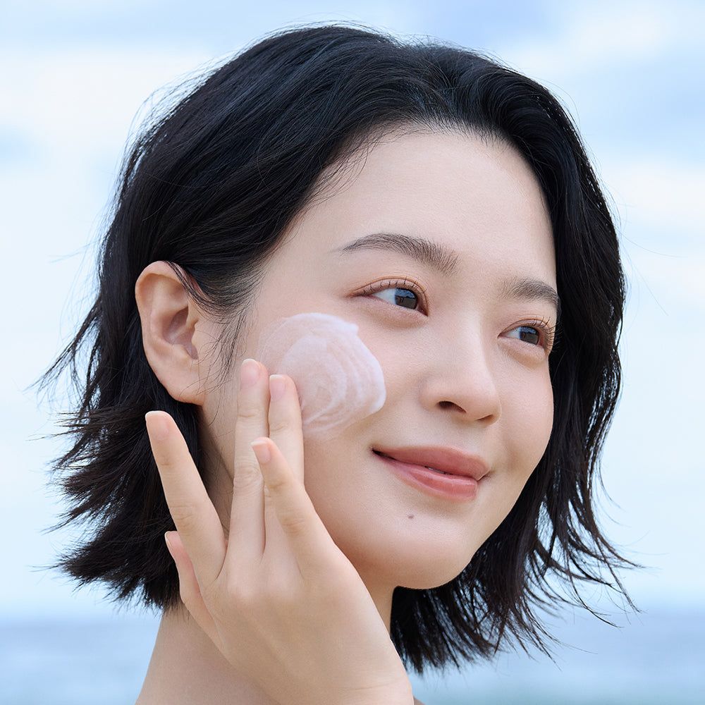 Viso di donna che applica una crema sulla pelle. Crema visibile. Nessuna denominazione del prodotto.