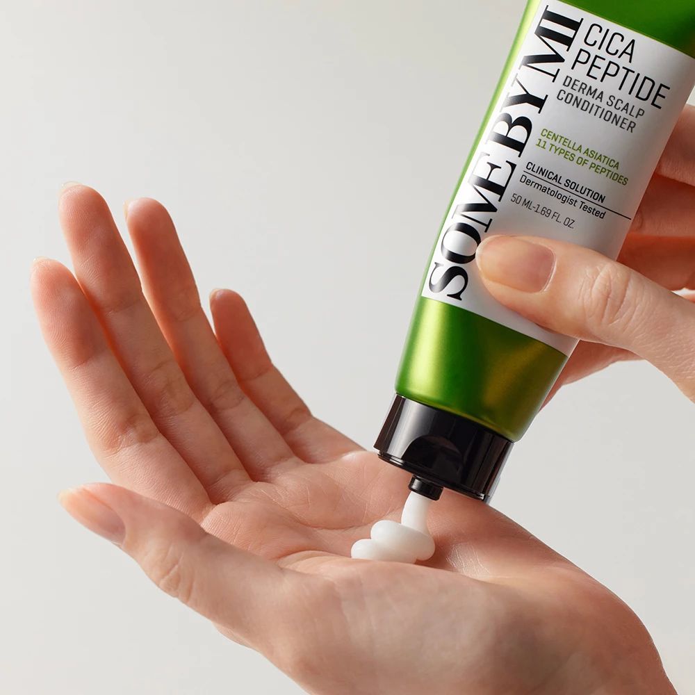 Tubo verde SOME BY MI Cica Peptide Derma Scalp Conditioner. Crema bianca spremuta nella mano.