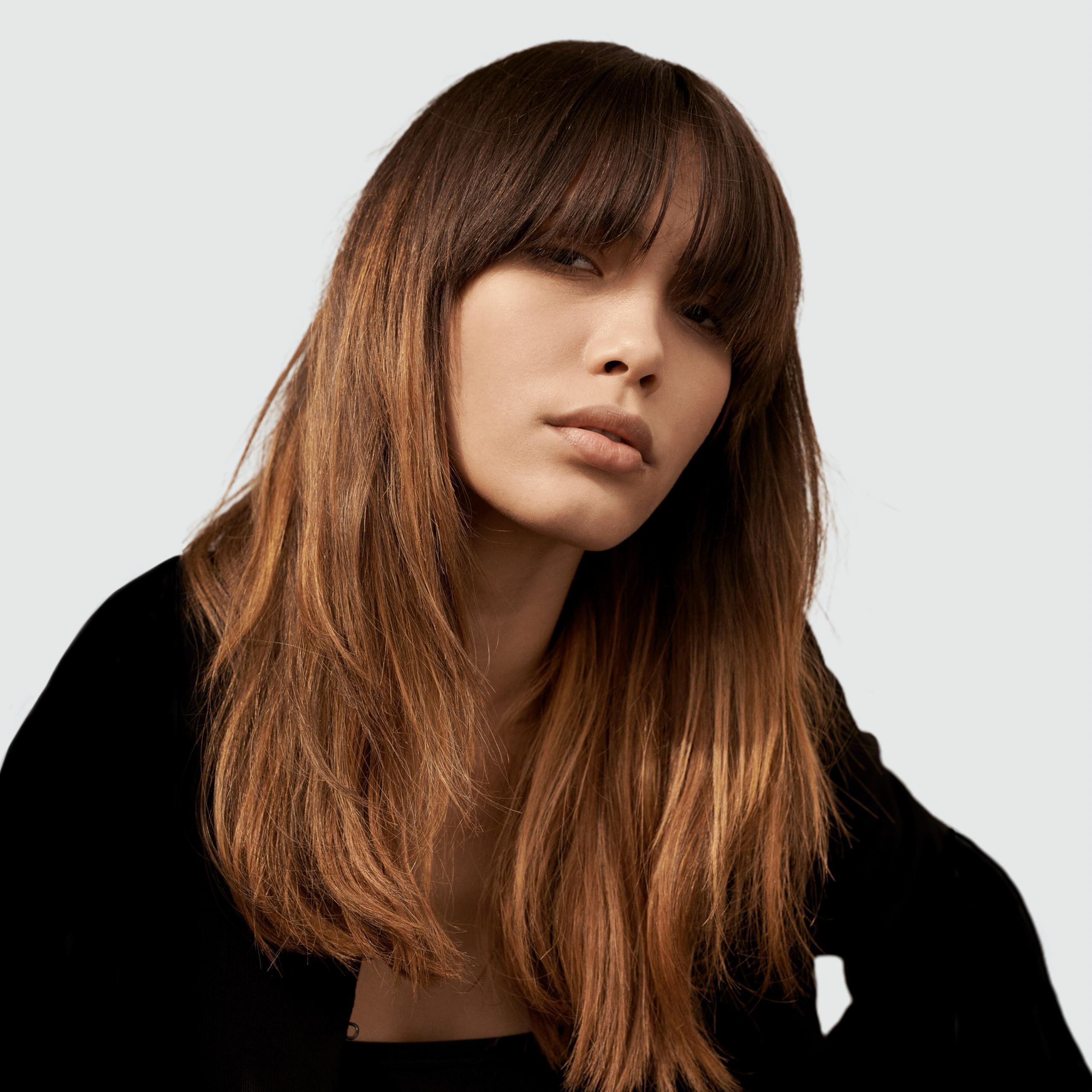 Ritratto di donna con capelli castani ondulati con frangia. Indossa un top nero.