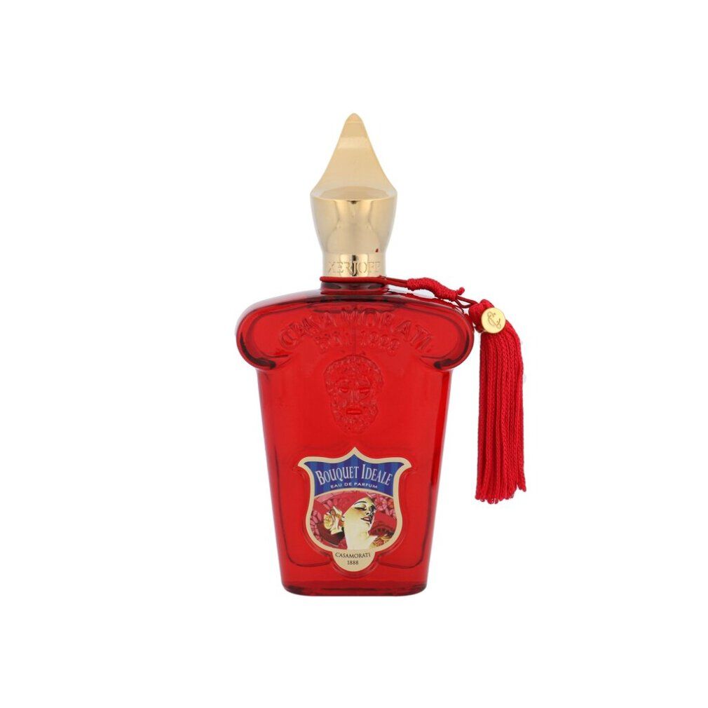 Flacone rosso con tappo dorato e nappa. Etichetta con motivo floreale e scritta.