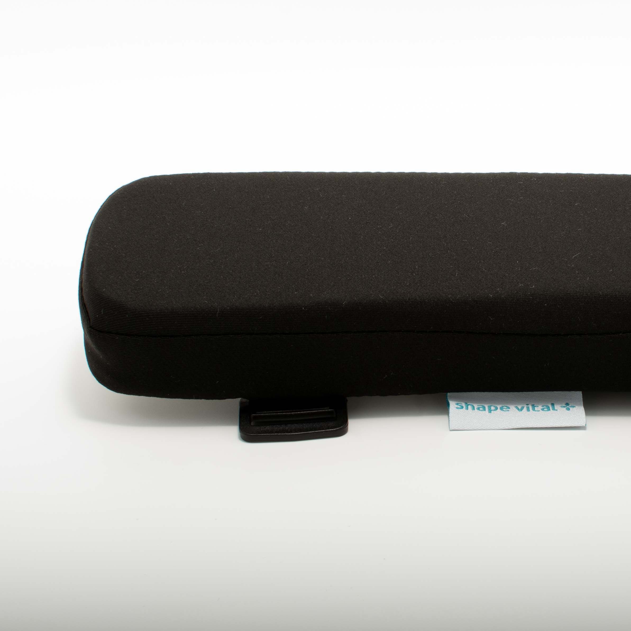Cuscino nero per bracciolo con angoli arrotondati. Piccola etichetta con 'shape vital+'. Clip di fissaggio nero.