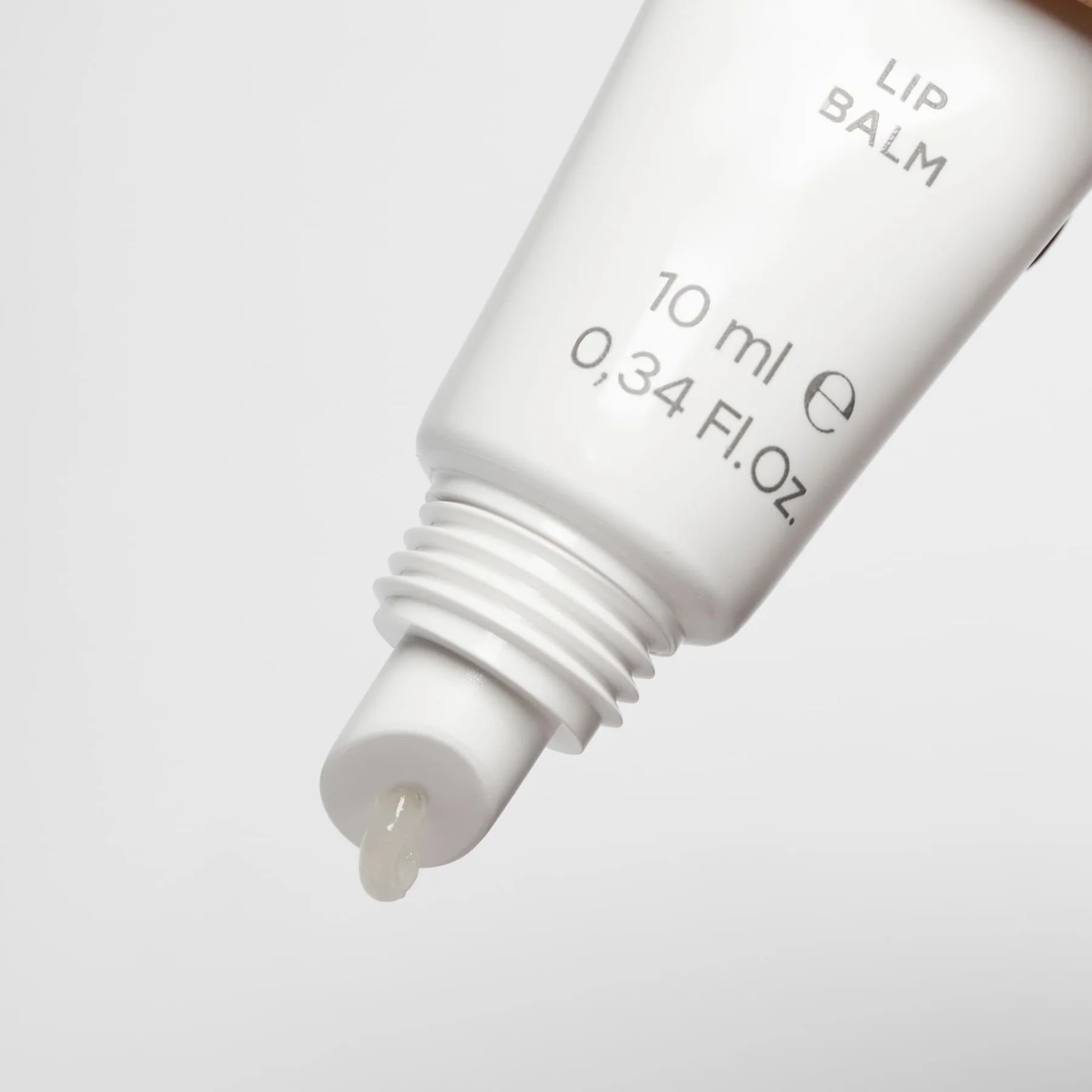 Primo piano di un tubo di balsamo per le labbra bianco. L'apertura mostra una piccola quantità di prodotto. Sul tubo è scritto "10 ml e 0,34 Fl.Oz.".