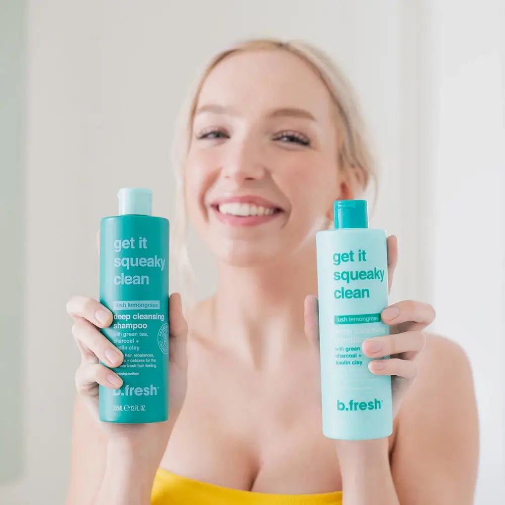Donna tiene due flaconi di shampoo verdi "Get it squeaky clean". Marchio: B.fresh. Scritta: Pulizia profonda.