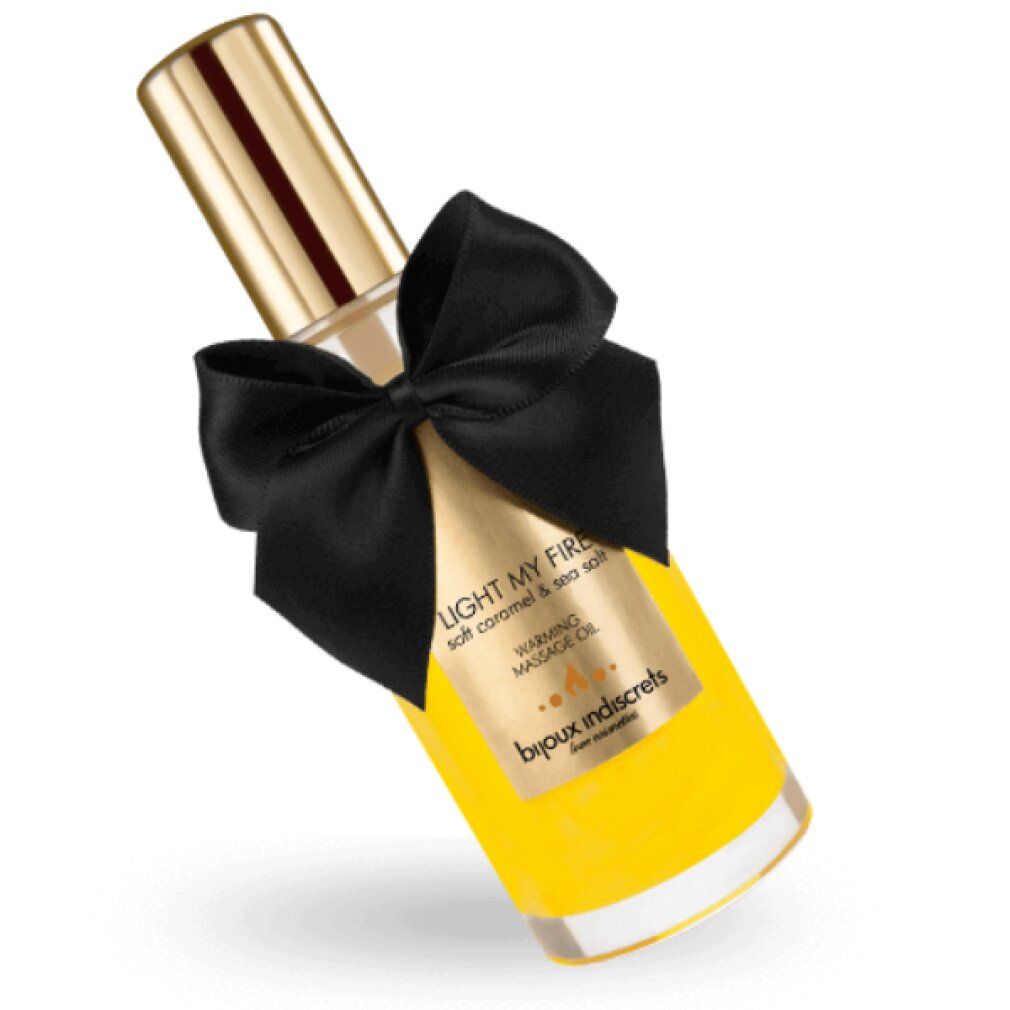 Flacone in vetro inclinato con tappo dorato, liquido giallo e fiocco nero. Scritta: Light My Fire, Warming Massage Oil.