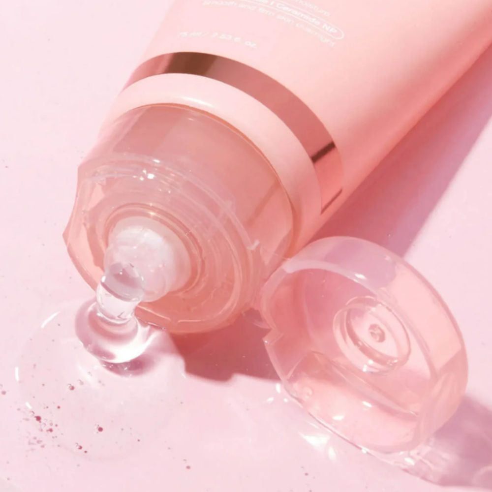 Primo piano di un tubo da cui esce un liquido trasparente. Sfondo rosa.