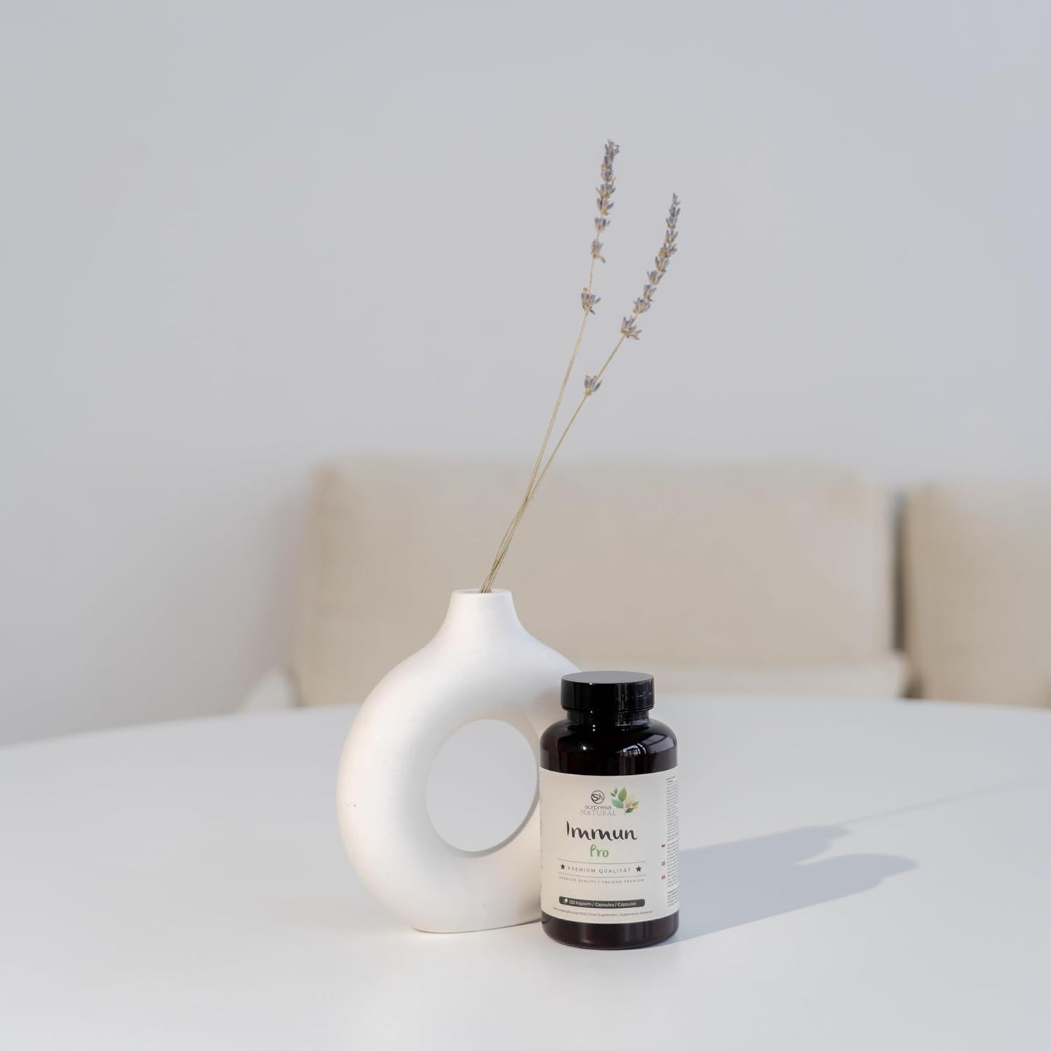 Flacone marrone Surpresa Natural Immun Pro su un tavolo bianco, accanto a un vaso con rami.