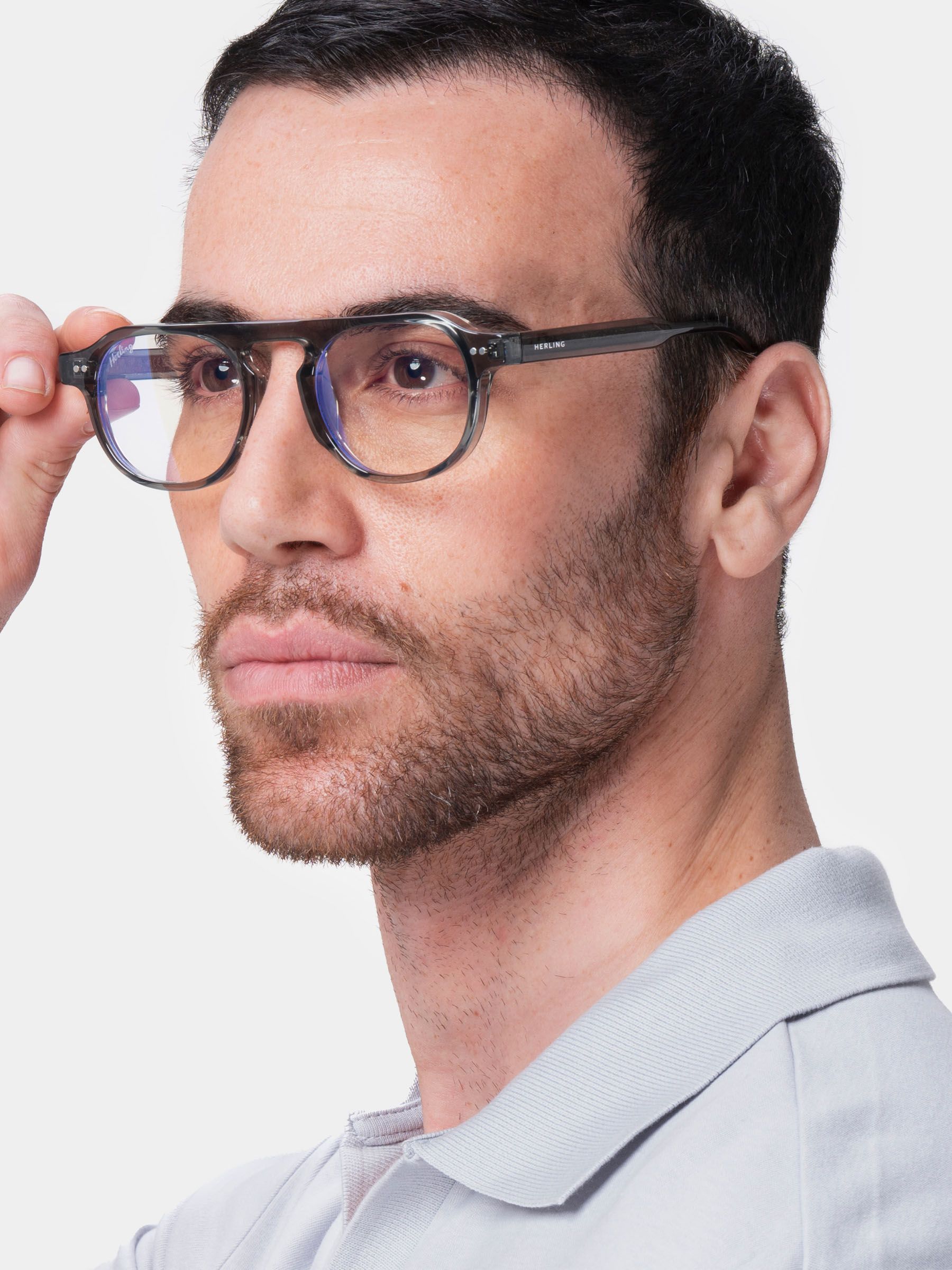 Uomo con occhiali grigi. Le lenti hanno una tonalità giallastra. L'uomo tiene gli occhiali. La montatura è grigia.