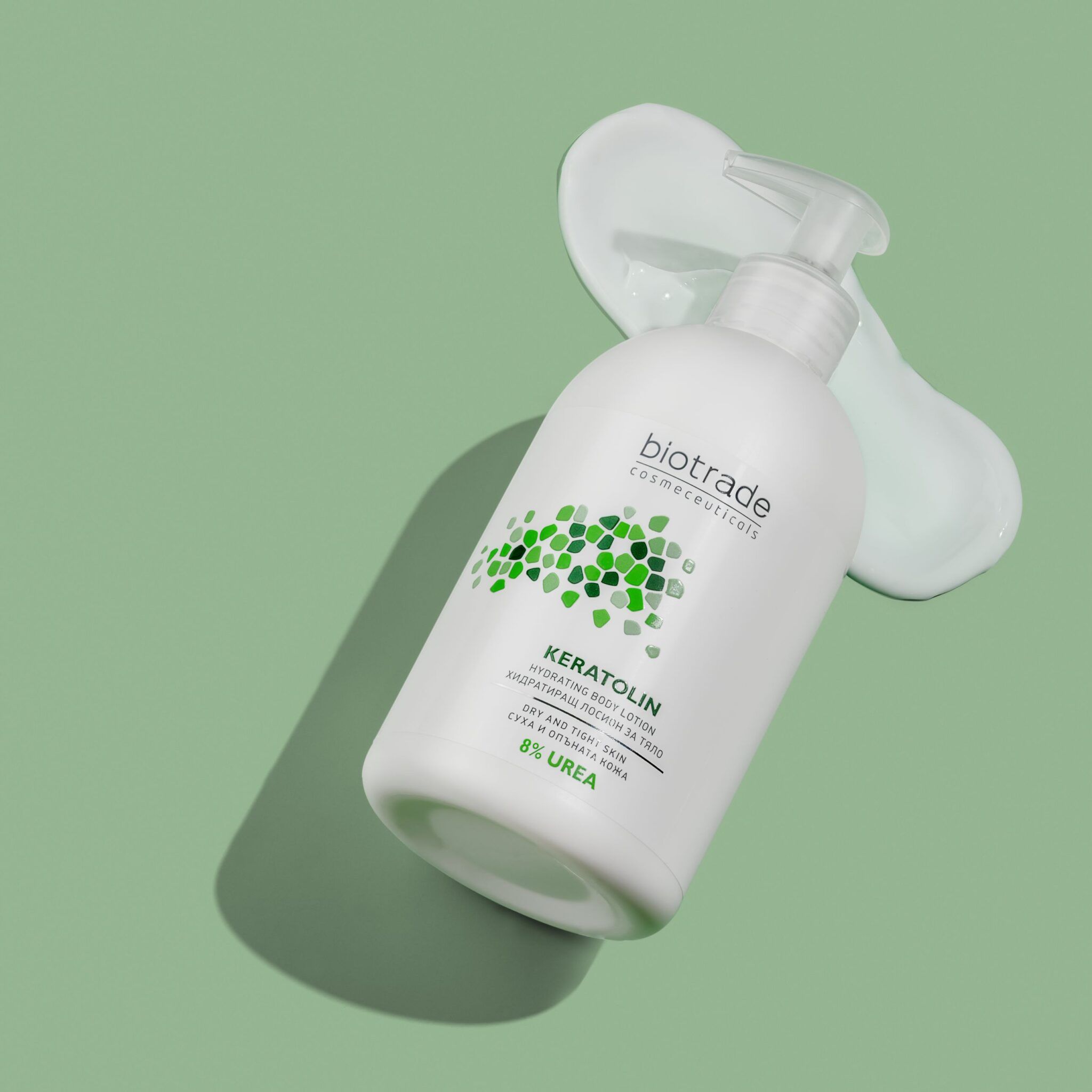 Flacone bianco con dosatore. Biotrade Keratolin Body, 8% Urea. Liquido verdognolo accanto. Su sfondo verde.