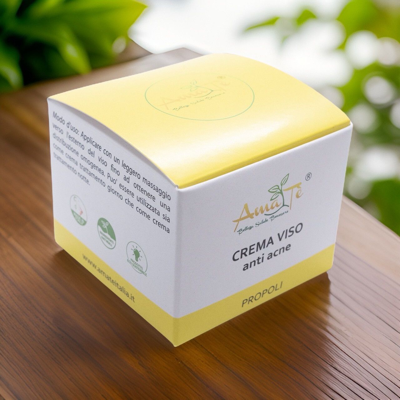 Scatola bianca e gialla su superficie in legno. Scritto: Crema viso anti acne, Propoli. Logo con foglie. Foglie verdi sullo sfondo.