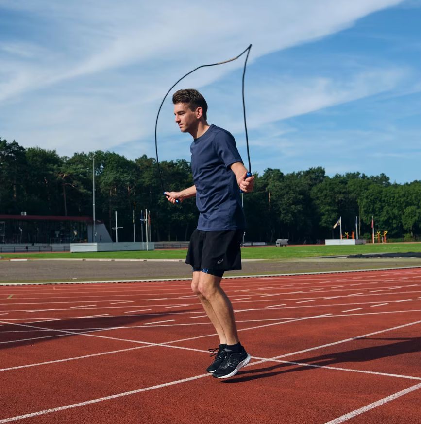 Uomo che salta con la corda su una pista rossa. Corda nera, manici blu.