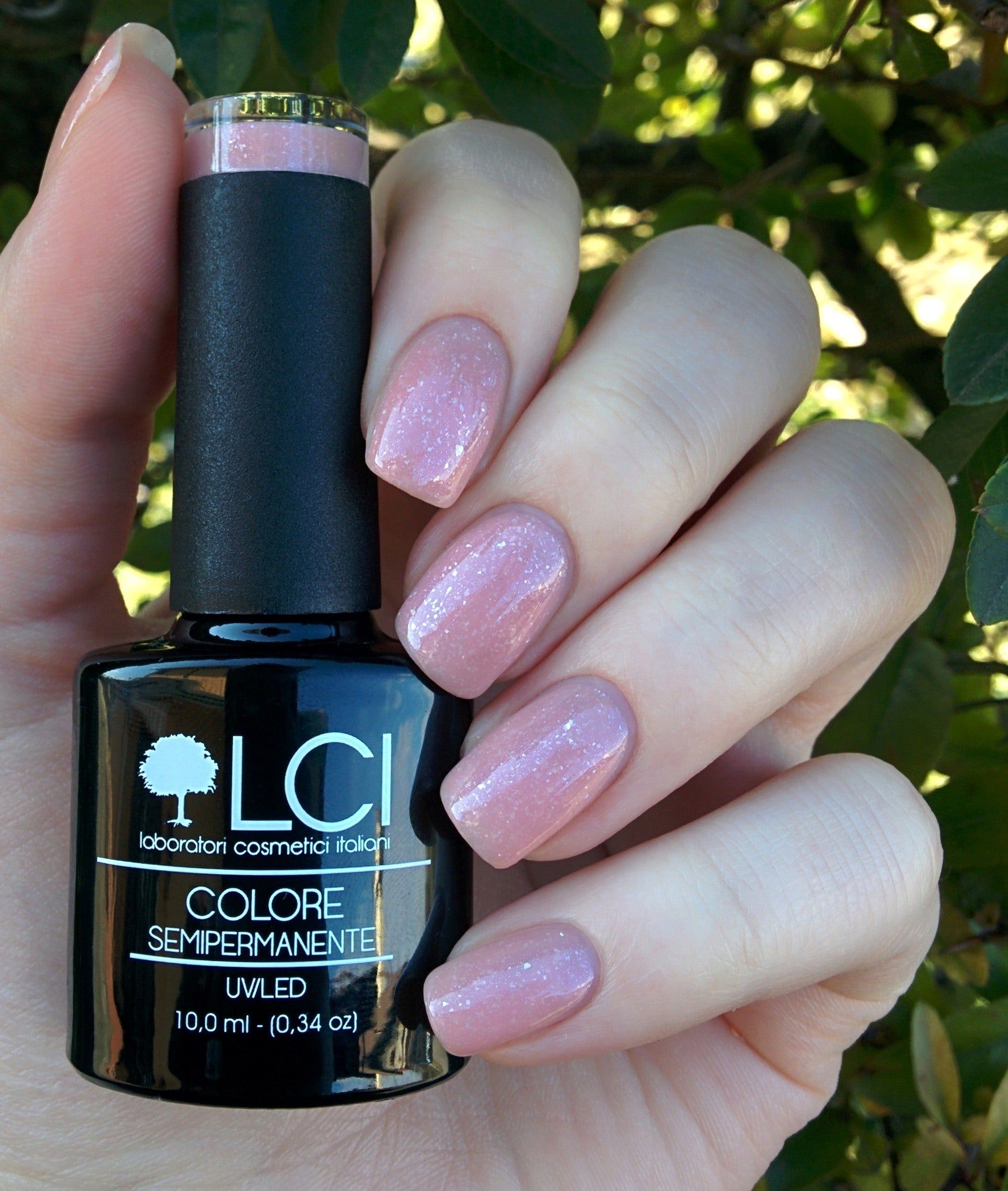 Flacone di smalto e unghie smaltate. Smalto rosa glitterato. Flacone nero con etichetta: LCI, Colore Semipermanente. Mano che tiene il flacone.