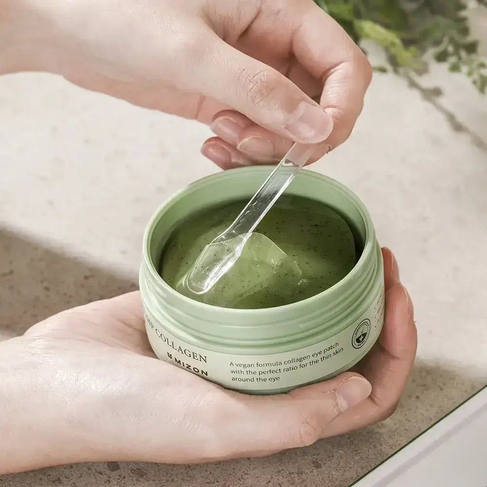 Mani con spatola in barattolo con patch in gel per occhi. Gel verde. Scritta: Phyto Plump Collagen Eye Gel Patch. Marchio: Mizon.