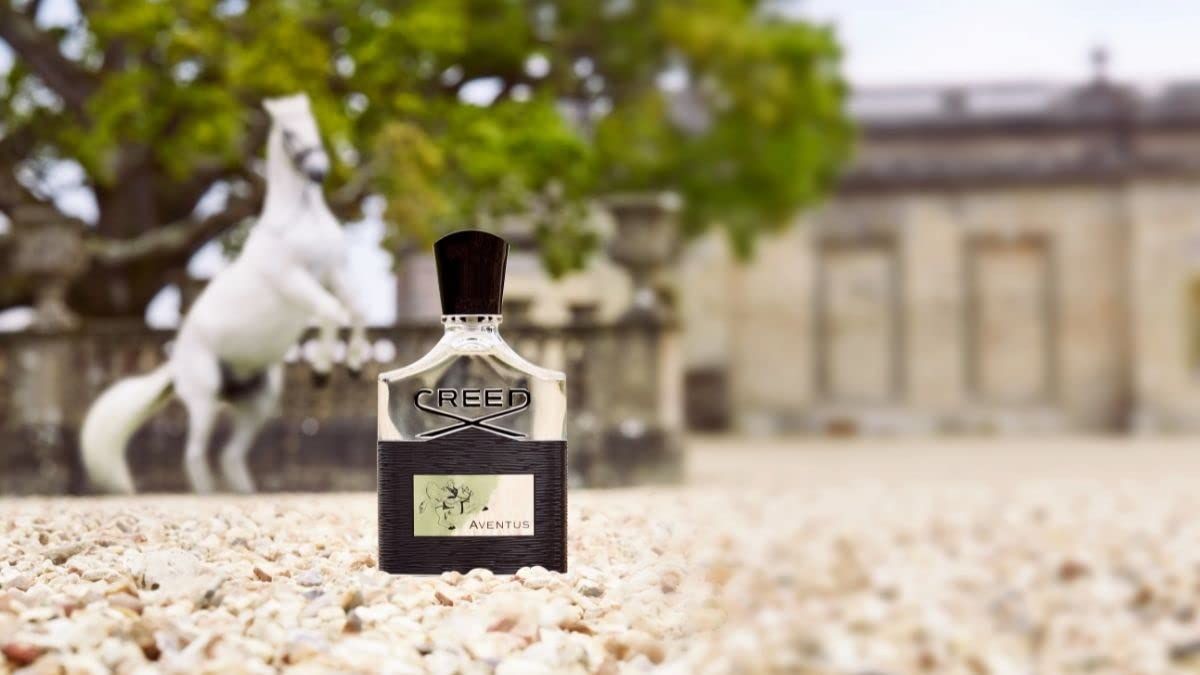 Flacone di profumo con etichetta nera e scritta bianca. Sullo sfondo un cavallo bianco e un edificio.