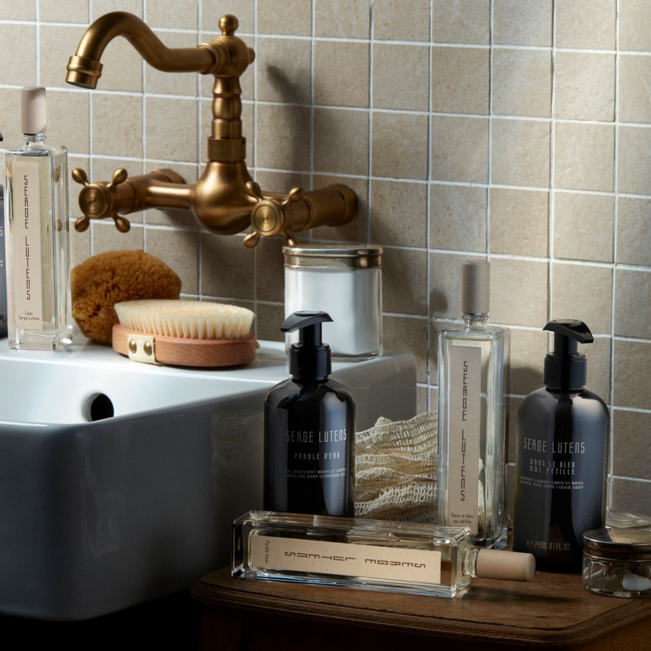 Diverse bottiglie e contenitori su un tavolo. Scritta: SERGE LUTENS. Flaconi neri con dosatore, flaconi rettangolari.