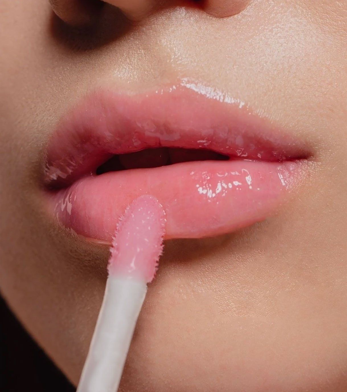 Primo piano di labbra che ricevono un lucidalabbra rosa applicato con un applicatore.