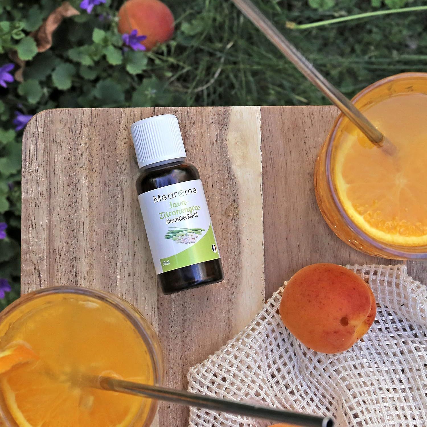 Flacone del prodotto su tagliere con bevande e albicocche. Etichetta del prodotto visibile. Cannucce nei bicchieri.