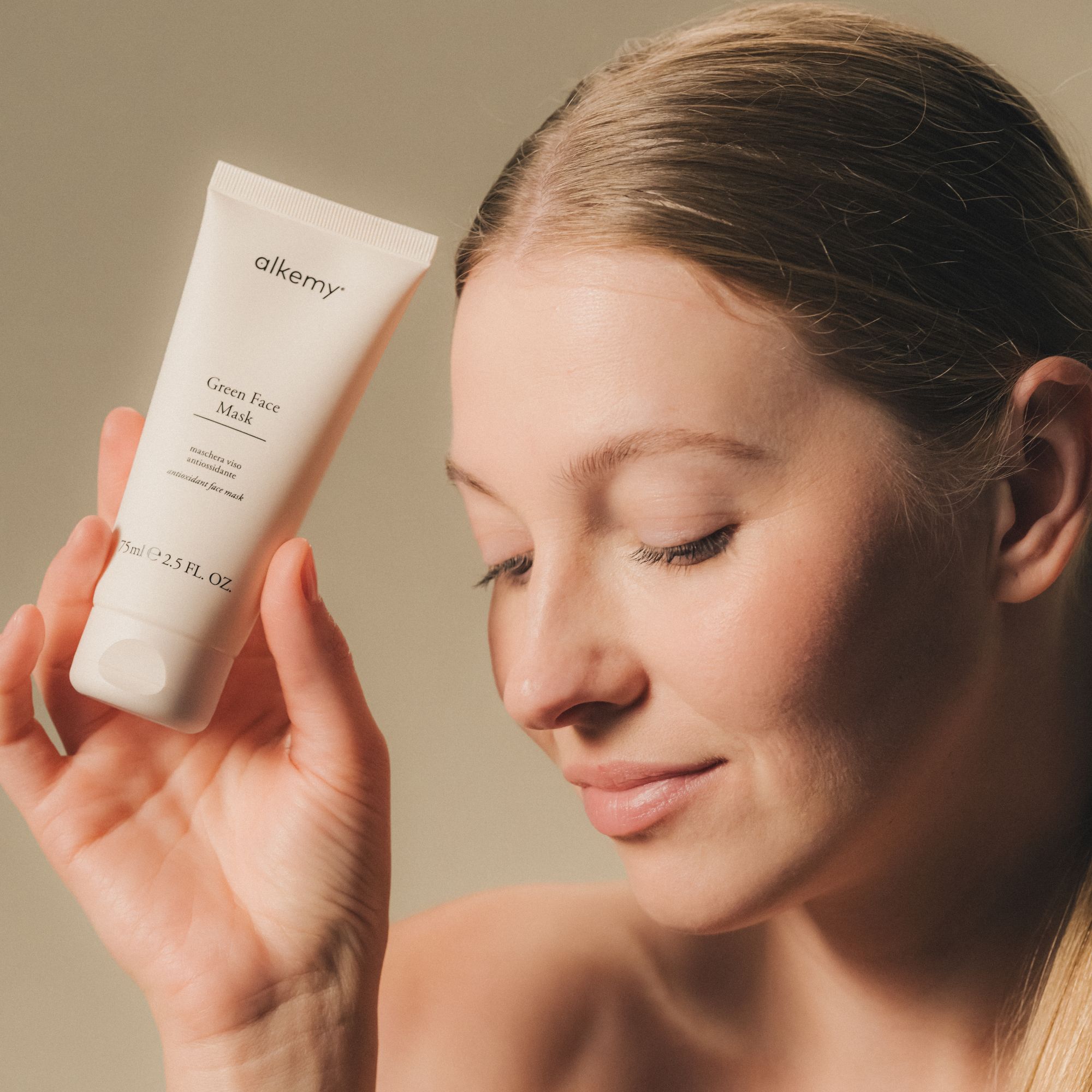 Una donna tiene in mano un tubetto bianco di Alkemy Green Face Mask.