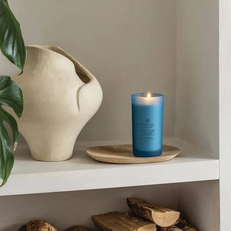 Candela blu accesa su vassoio di legno. Chesapeake Bay, mind & body, confidence + freedom. Su mensola.