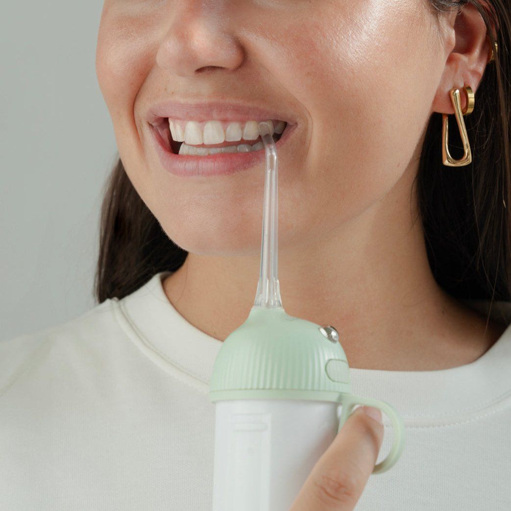 Primo piano di una persona che usa un idropulsore. Beccuccio in bocca. Orecchini dorati.