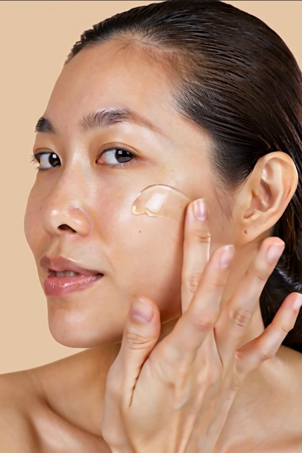 Donna applica siero sul viso. Pelle chiara, capelli castani, sfondo beige.