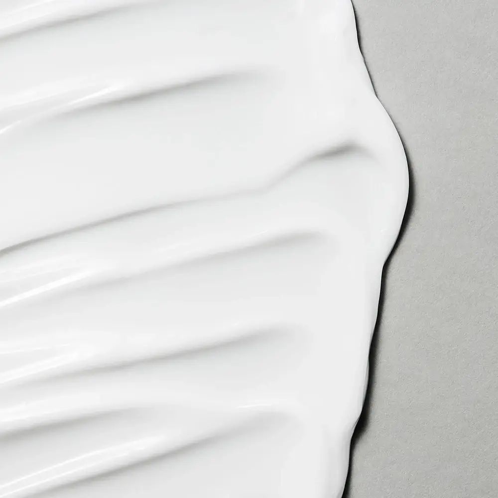 Primo piano di crema bianca su sfondo grigio. La crema è applicata a onde.