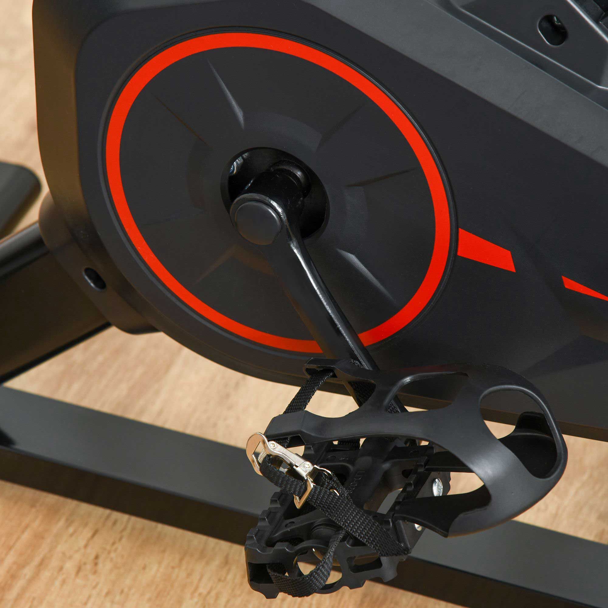 Primo piano dei pedali di una bicicletta fitness. Colore nero con cinghie. Su pavimento in legno.