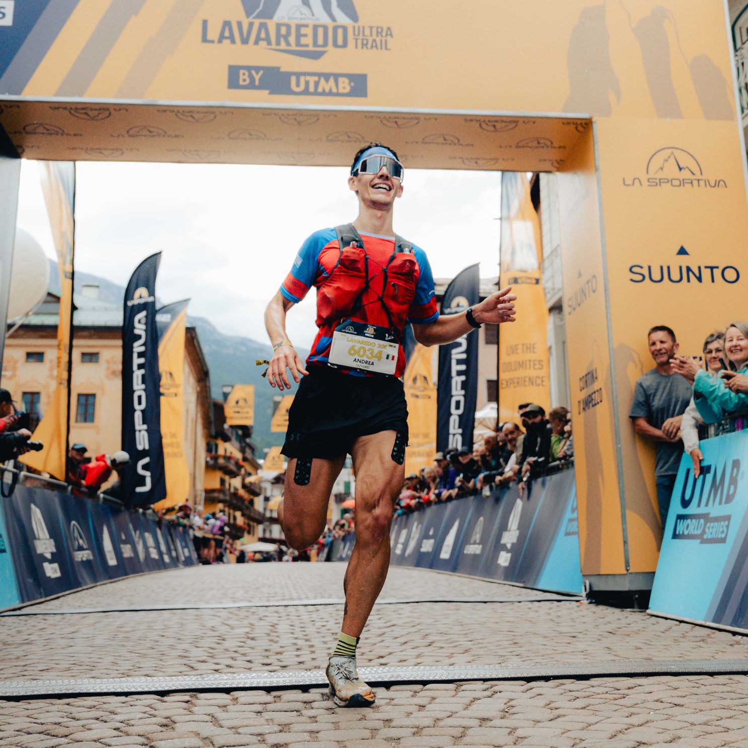 Corridore taglia il traguardo. Banner con testo: LAVAREDO ULTRA TRAIL. Logo: UTMB WORLD SERIES. Atleta con cerotti sportivi.
