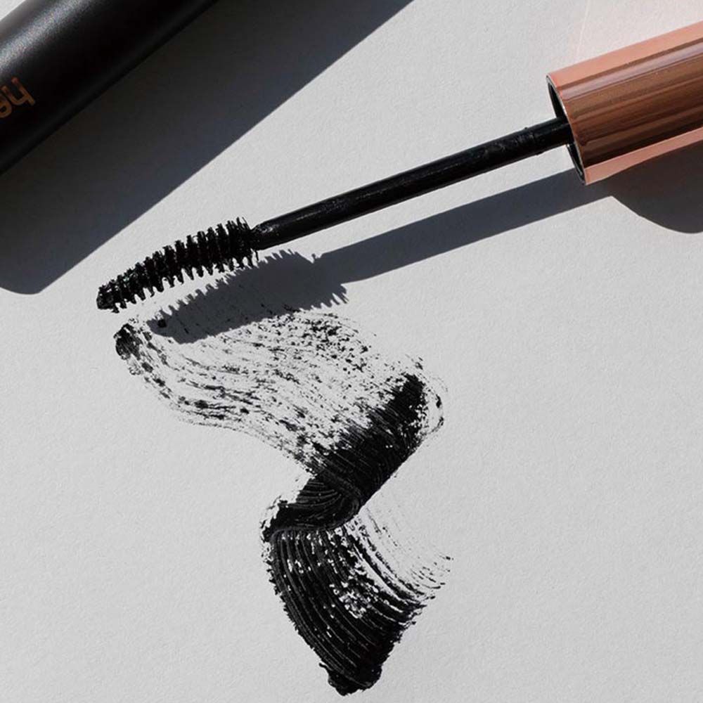 Applicatore di mascara con spazzola e traccia di mascara nero su carta bianca. L'applicatore ha un cappuccio color rame.