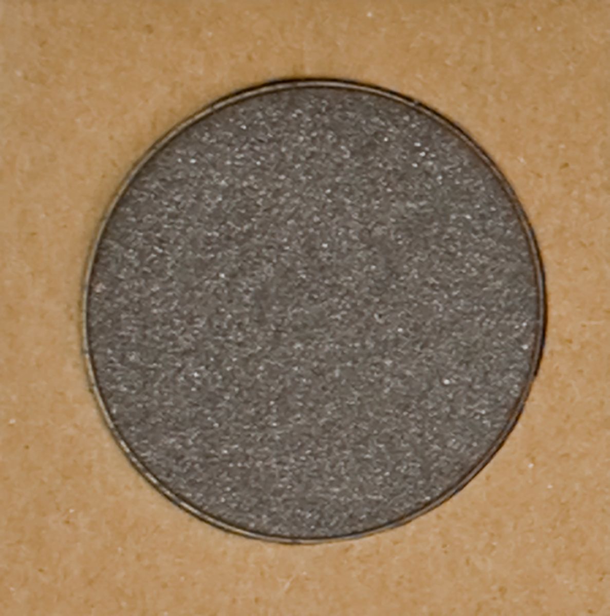 Ombretto grigio rotondo in un contenitore marrone. L'ombretto ha una superficie scintillante.