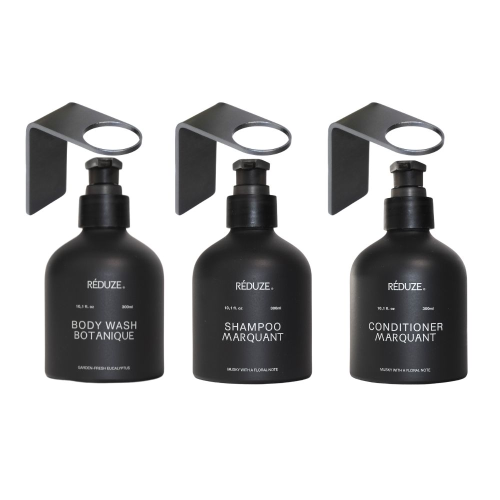 Tre flaconi neri con dispenser e supporti a muro. Etichette: Body Wash, Shampoo, Conditioner. Marchio: RÉDUZE.