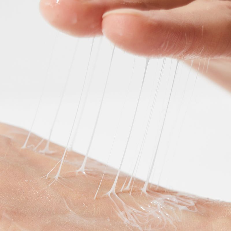 Primo piano di una mano che applica una sostanza cremosa sulla pelle. La crema forma dei fili.