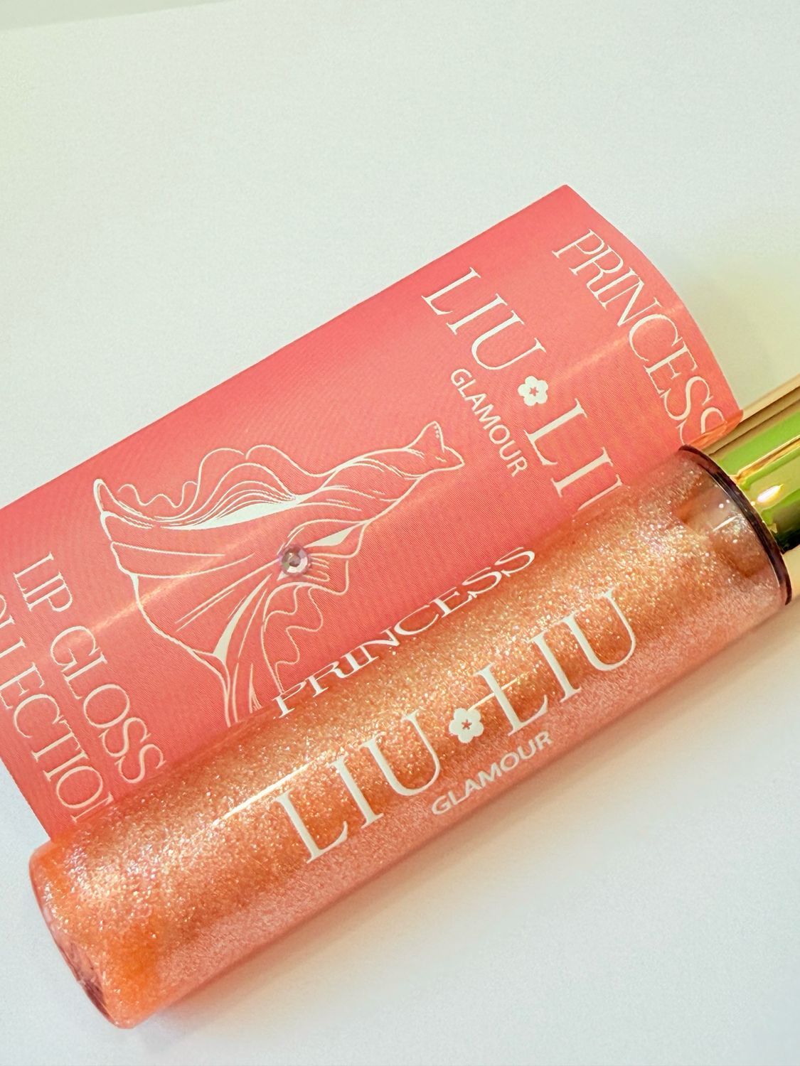 Lucidalabbra rosa glitterato con tappo dorato. Scritta: PRINCESS LIU LIU Glamour. Confezione rosa sullo sfondo.