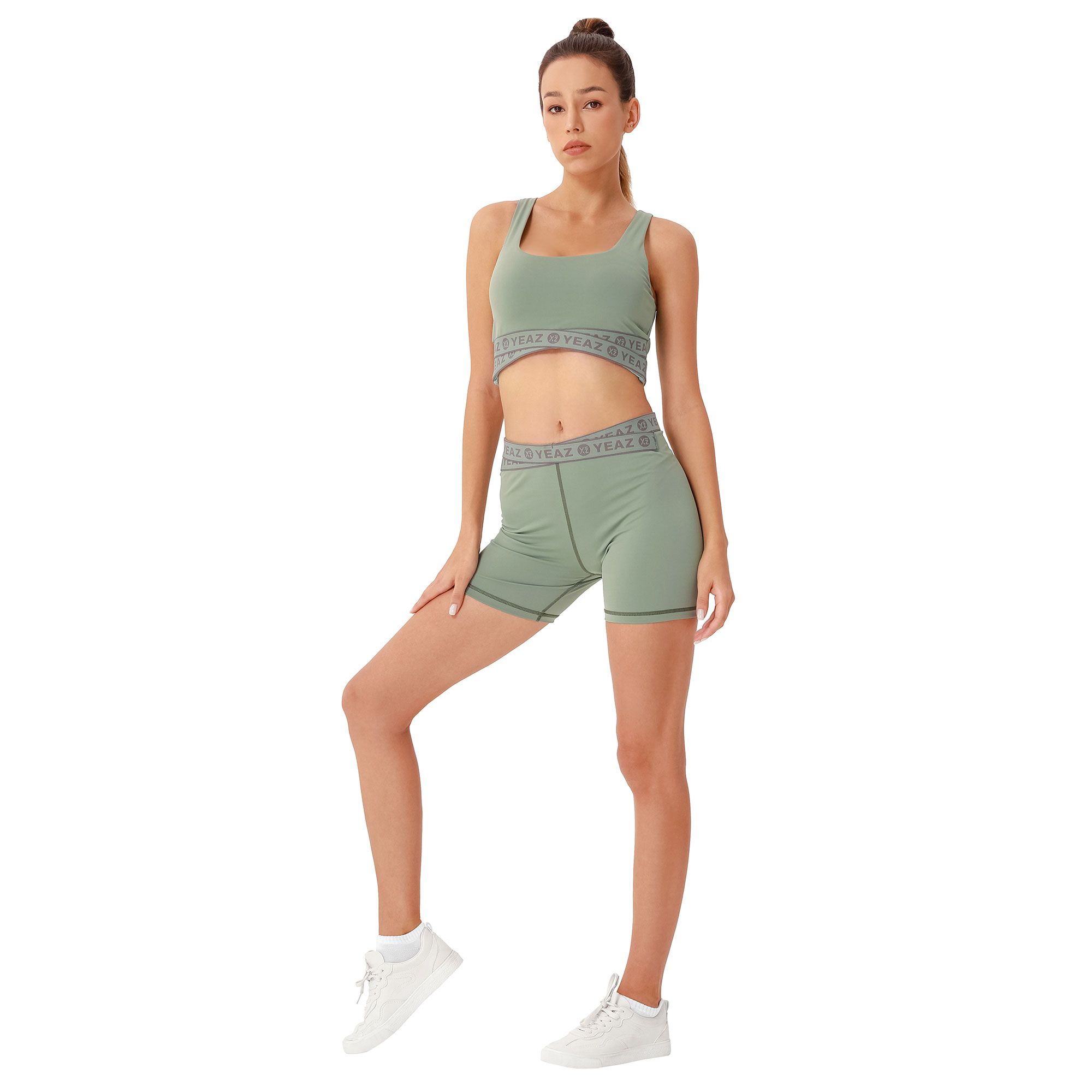 Donna in un completo sportivo verde a due pezzi: crop top e pantaloncini da ciclista con fascia grigia.