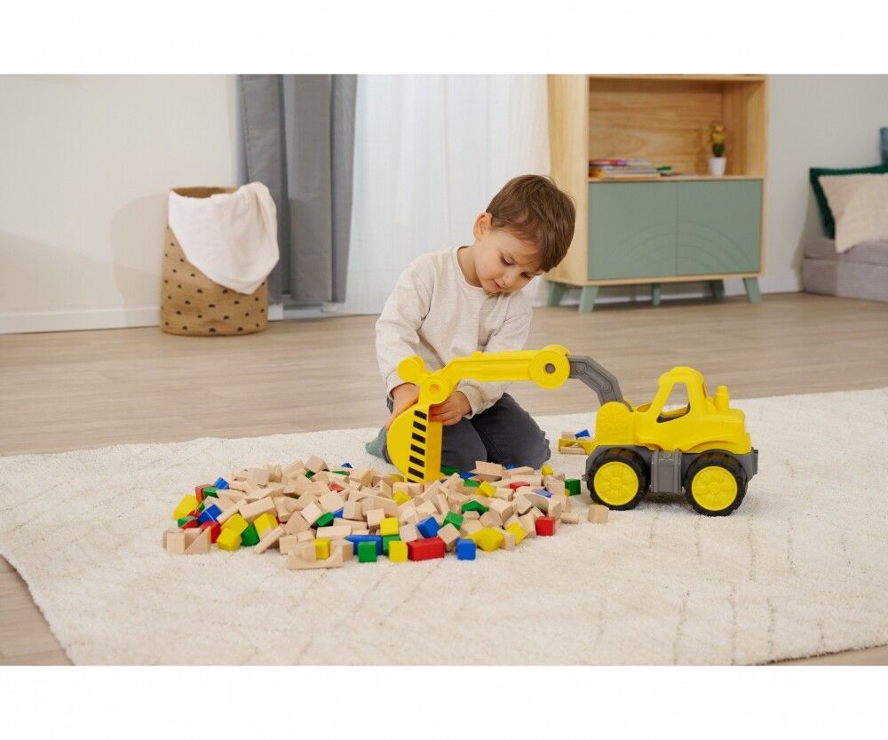 Bambino che gioca con un escavatore giallo e blocchi di legno su un tappeto. Escavatore con strisce nere sulla benna.