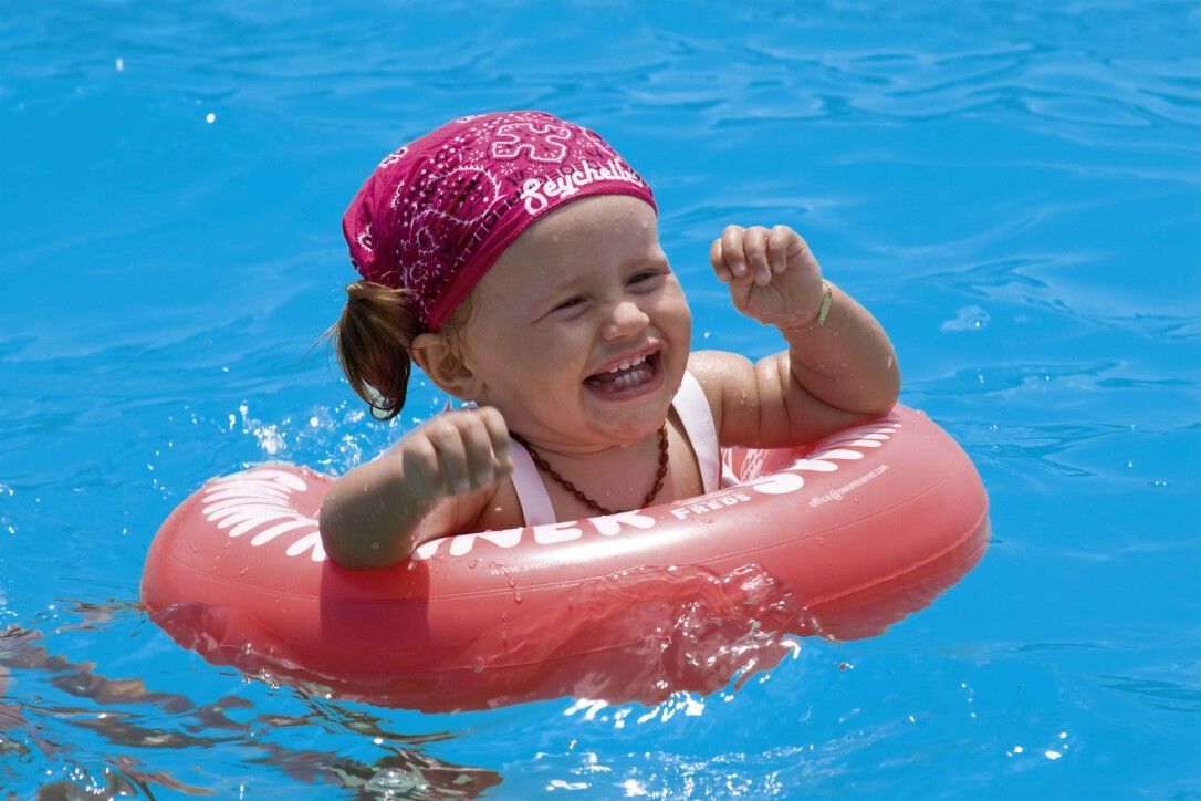 Bambino in Schwimmtrainer rosso in piscina. Marchio Freds Swim Academy. Il bambino indossa un foulard.