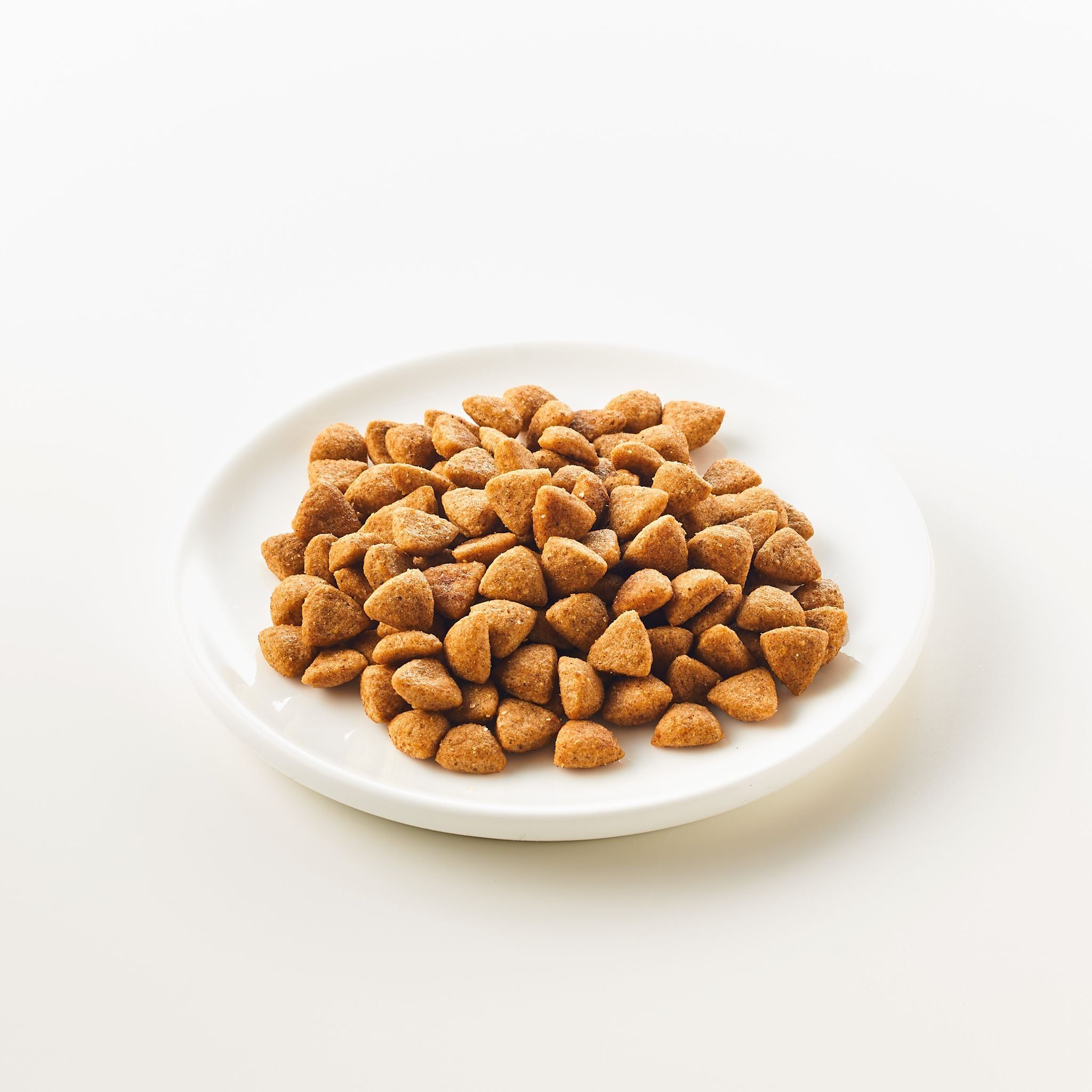 Mucchio di crocchette triangolari marroni su un piatto bianco. Su sfondo chiaro.