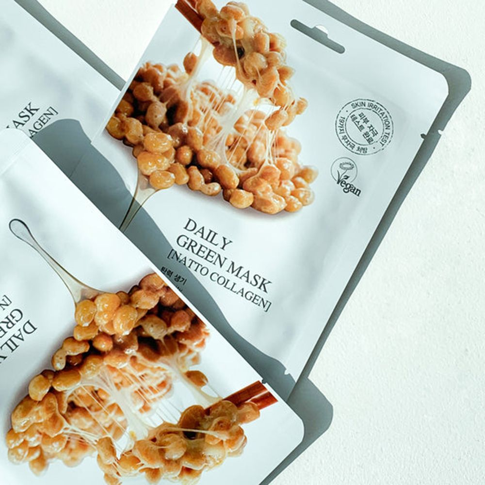 Due confezioni bianche di maschera con immagine di fagioli natto. Testo: Daily Green Mask, Natto Collagen. Sigillo vegano.