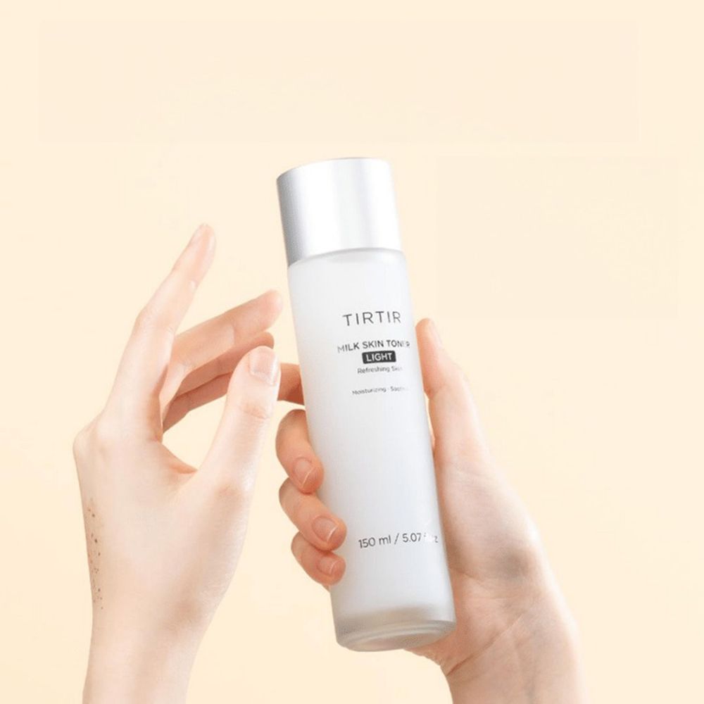 Mani che tengono TIRTIR Milk Skin Toner Light. Flacone bianco, tappo argento. Testo: Moisturizing, Soothing. 150 ml.