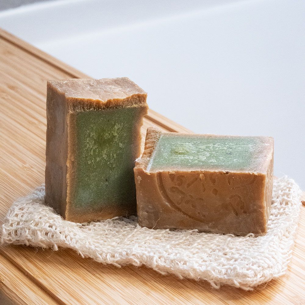 Due saponette rettangolari, interno verde. Su un guanto da toilette. Su tavola di legno.