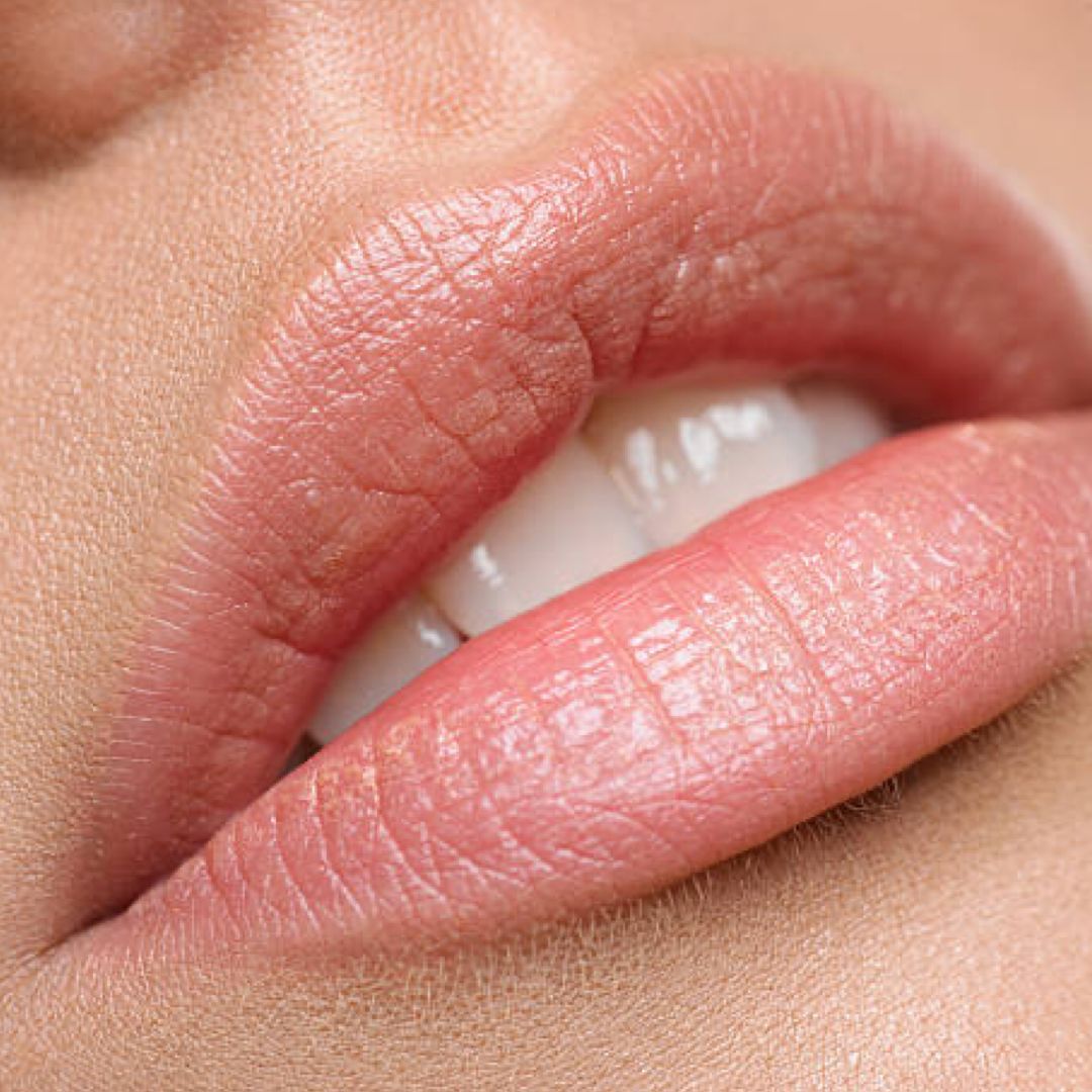 Primo piano di labbra. Labbra leggermente aperte, denti visibili. Labbra trattate con balsamo colorato.