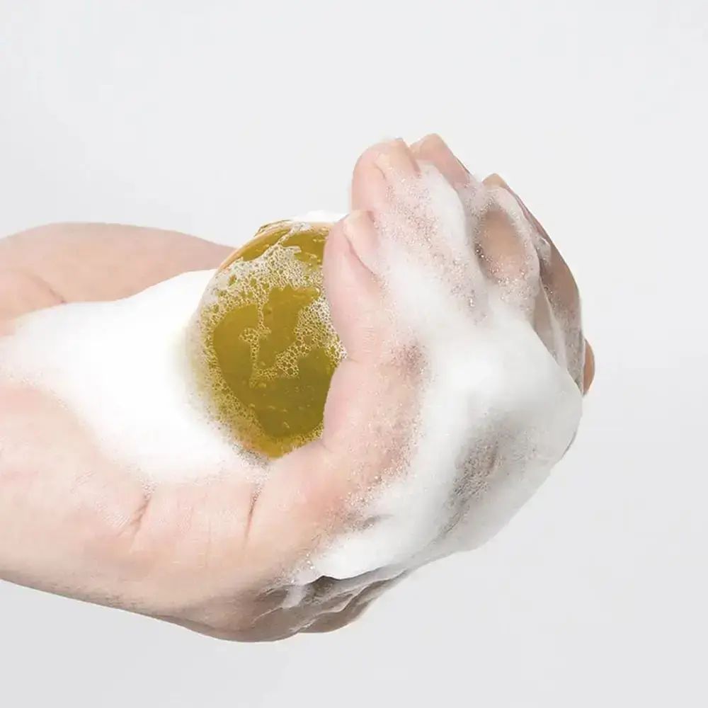 Mano che tiene una sfera gialla con schiuma. Su sfondo bianco.