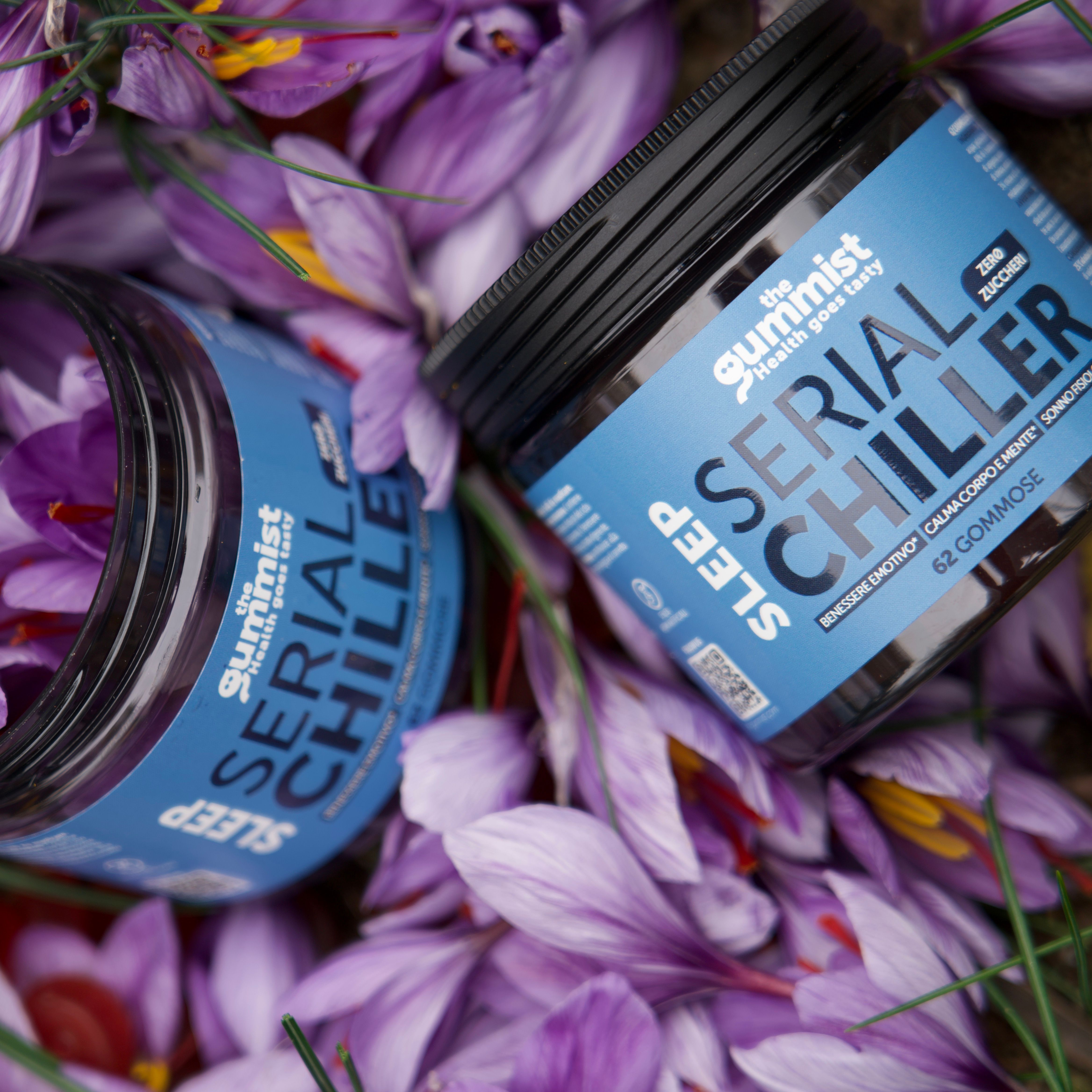 Due barattoli scuri con etichetta blu 'Serial Chiller' su petali viola.