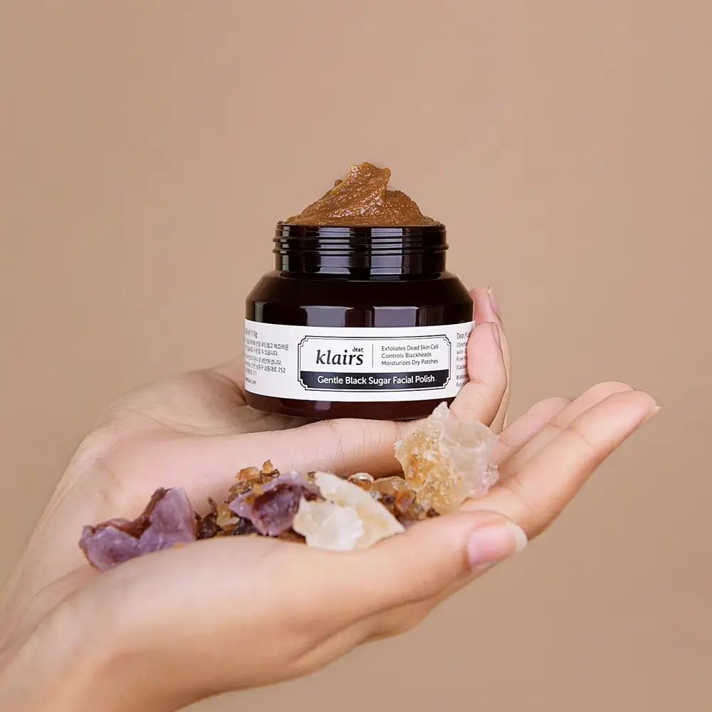 Vasetto di pasta esfoliante allo zucchero marrone. Cristalli nel palmo. Scritta: Dear Klairs Gentle Black Sugar Facial Polish.