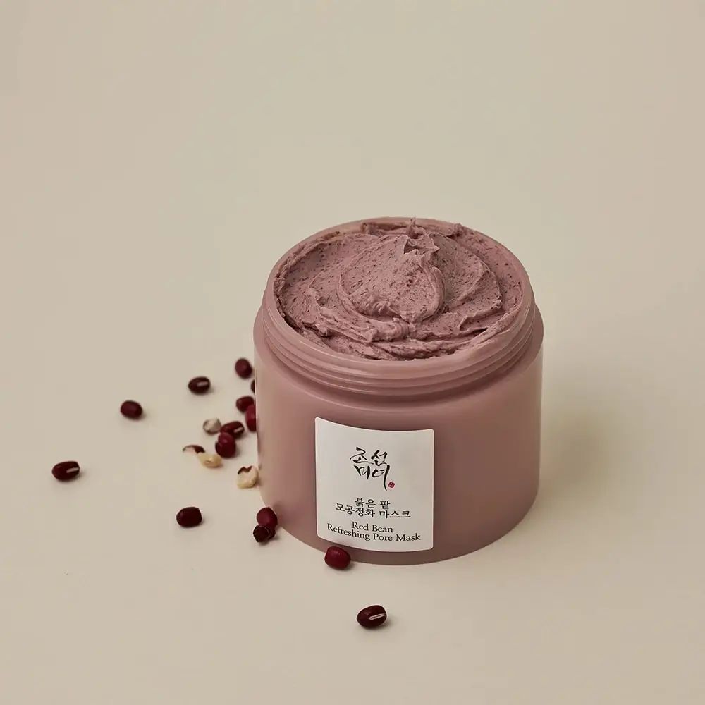 Vaso rotondo con contenuto rosa e coperchio bianco. Scritte: caratteri coreani, Red Bean Refreshing Pore Mask. Fagioli rossi accanto.