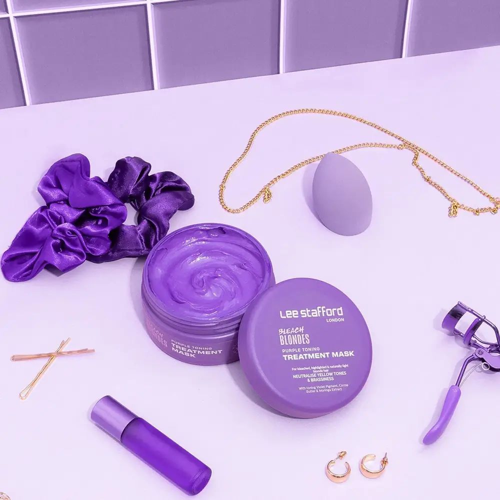 Vaso di maschera per capelli viola aperto. Accessori: elastico, catena, spugna, arricciaciglia, forcine, rossetto e orecchini.