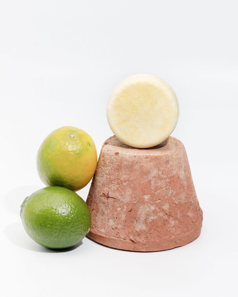 Docciaschiuma solido rotondo color crema su vaso terracotta. Agrumi accanto.