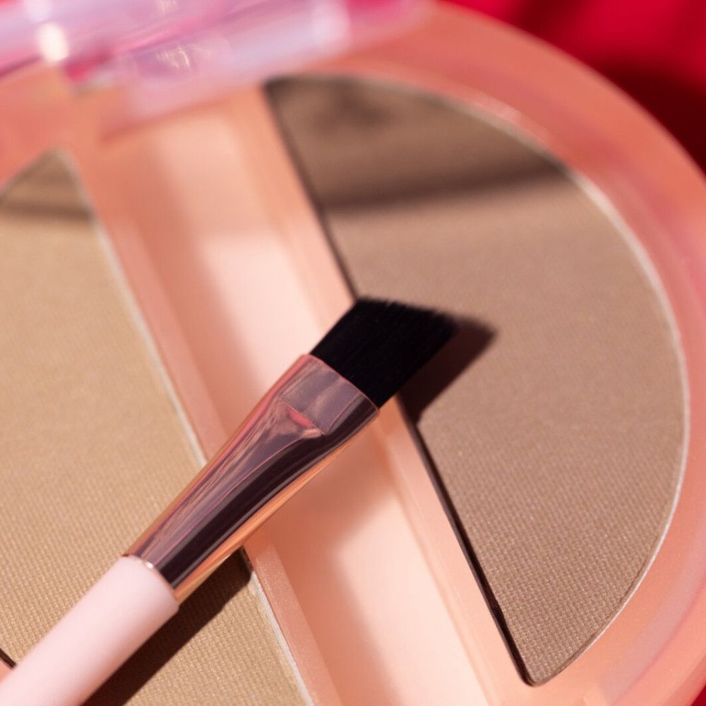 Primo piano del duo di polveri per sopracciglia. Pennello con testina a setole nere. Confezione rosa. Tonalità marroni.