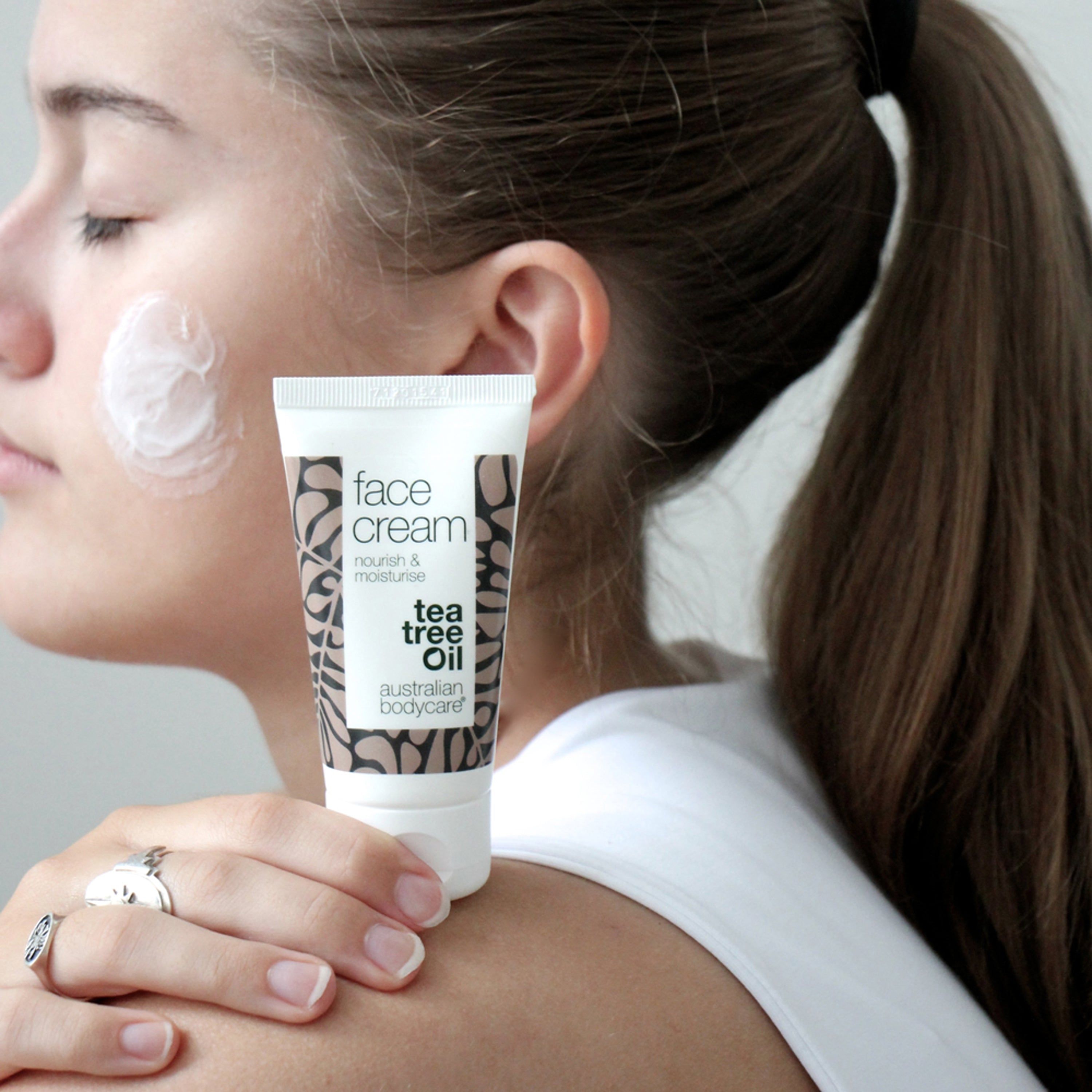Donna con crema sulla guancia. Tubo con testo: face cream, tea tree oil. Marchio: Australian Bodycare.