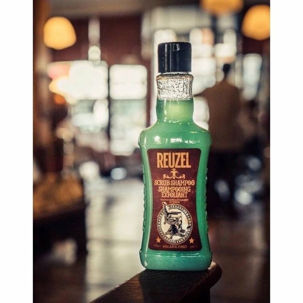 Flacone verde con tappo nero. Etichetta marrone con "REUZEL" e "SCRUB SHAMPOO". Logo con poltrona da barbiere.